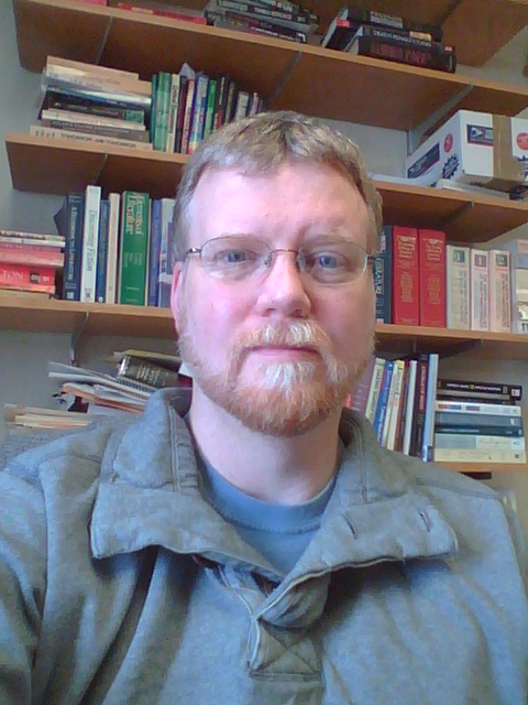 Headshot of person looking at camera in front of bookshelf.