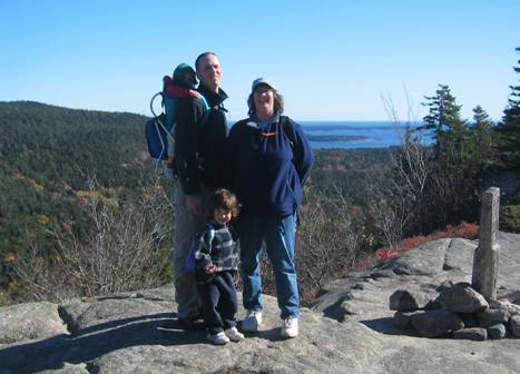 Woman, man, and small child standing on top of a mountain overlooking the coast