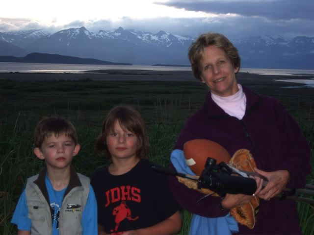 Woman and two children standing in front of flat marshland, with water and mountains behind