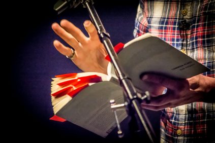 new writing series picture of speaker holding book and gesturing with hand in front of a mic